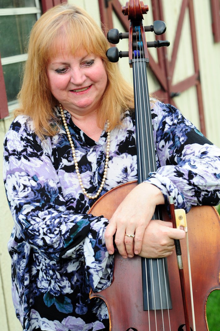Laurie leaning on her cello outdoors, smiling